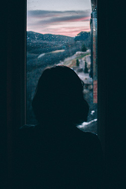 A silhouette of a woman gazing out into a vast, mountainous and foggy distance.