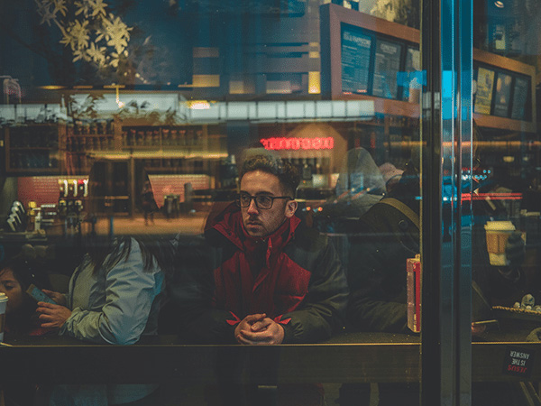 Depressed man sitting at a table looking out of a storefront window.