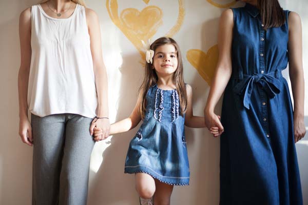 Same-sex couple with daughter holding their hands while standing in between them.  