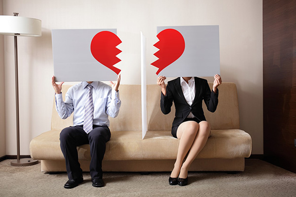 Couple sitting on couch holding two pieces of a heart with a divider between them.