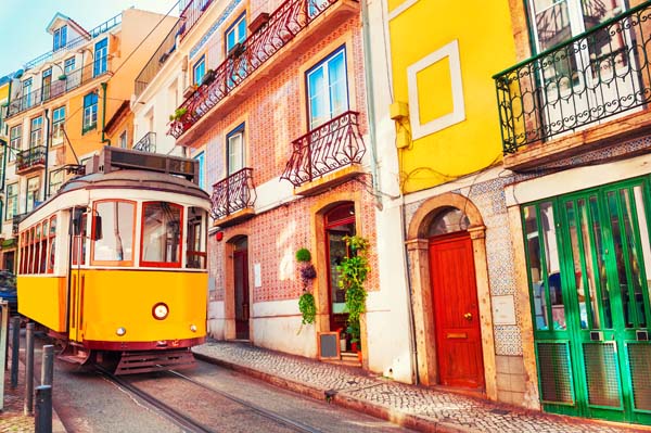 Yellow tram car traveling down a colorful, narrow street in Lisbon. 
