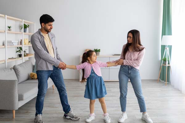 Mom and dad playing tug-of-war with daughter while standing in the living room.