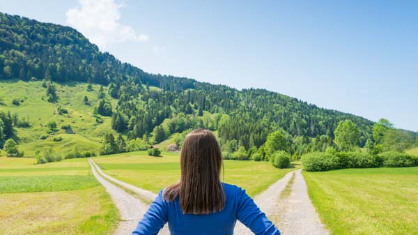Woman standing in front of two dirt paths deciding which way to go.