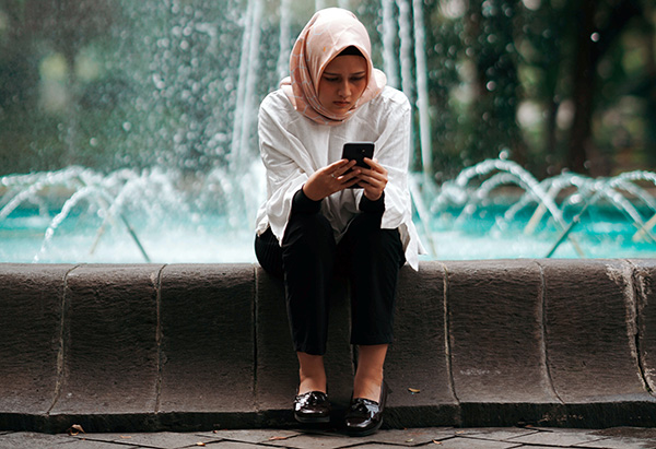 Girl sitting on fountain looking at phone.